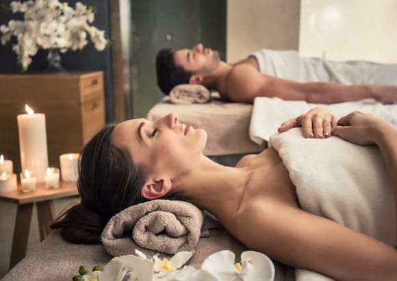 - Tranquil A couple enjoying an in-home couples massage on massage beds, with white sheets and candles.