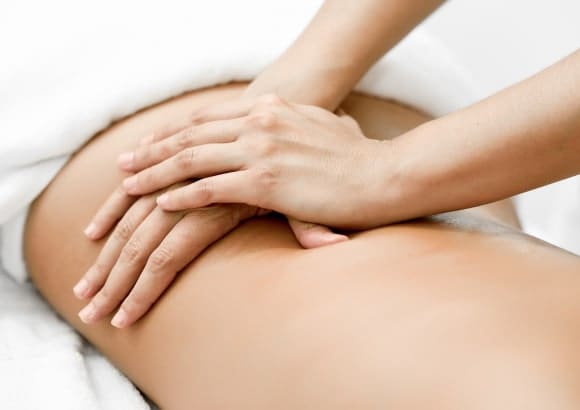 Woman lying face down, draped in a white blanket, receiving a Swedish massage on her back