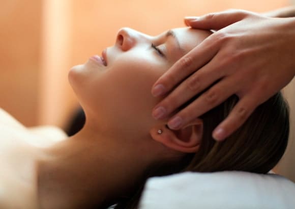 Woman receiving a gentle head massage, lying face up on a white pillow